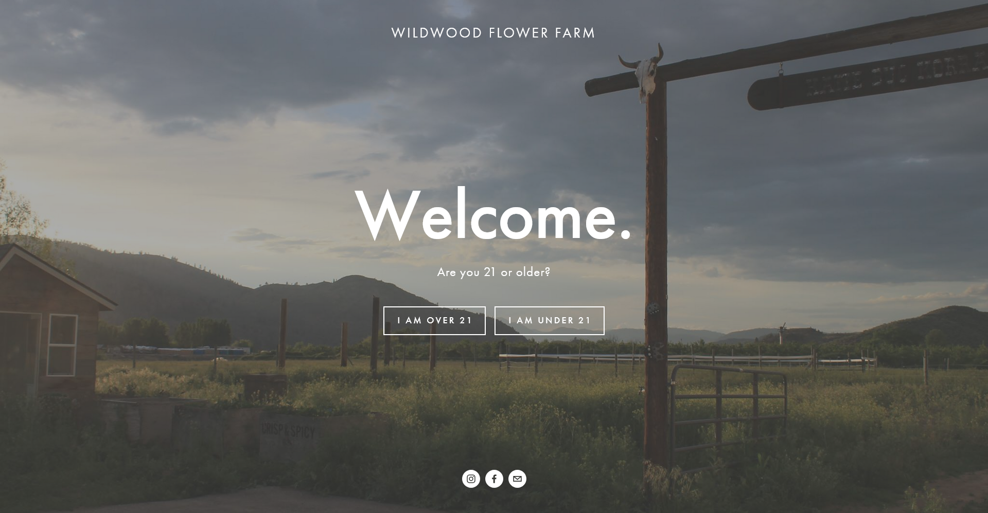 Wildwood Flower Farm website age-gate landing page: 'Welcome.' over a dusk photograph of the Okanogan farm with mountains, fields, and a weathered sign post.